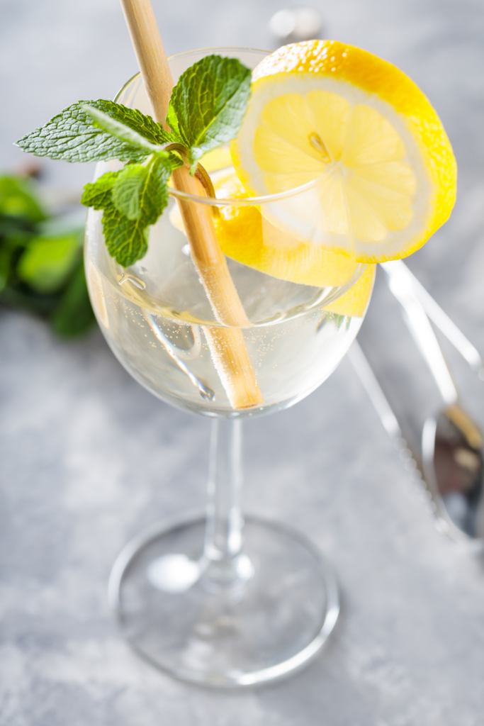 A crisp and refreshing Elderflower Spritz served in a stemmed wine glass with effervescent bubbles. The drink is garnished with a fresh lemon slice and a sprig of mint, adding a bright citrus and herbal touch.